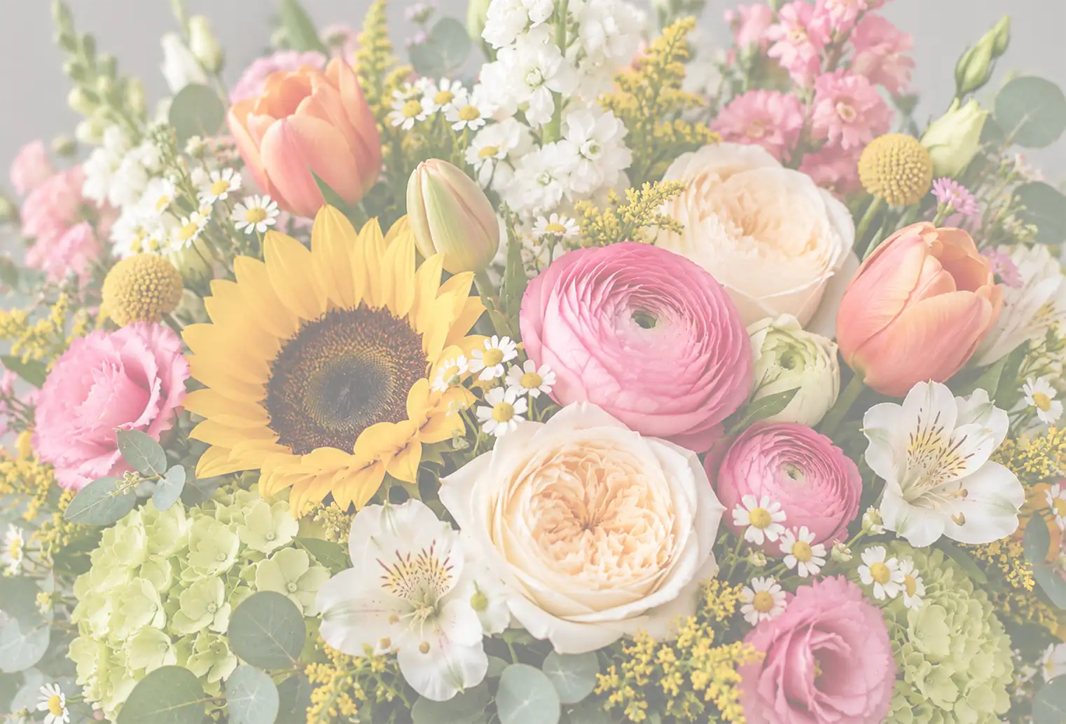 Close-up of a lush mixed flower arrangement featuring a large sunflower, pink ranunculus, peach garden roses, coral tulips, white stock, green hydrangeas, white daisies, yellow filler flowers, and eucalyptus greenery in Niantic, Connecticut